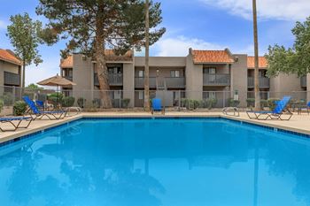 A swimming pool in front of a building with blue chairs around it.